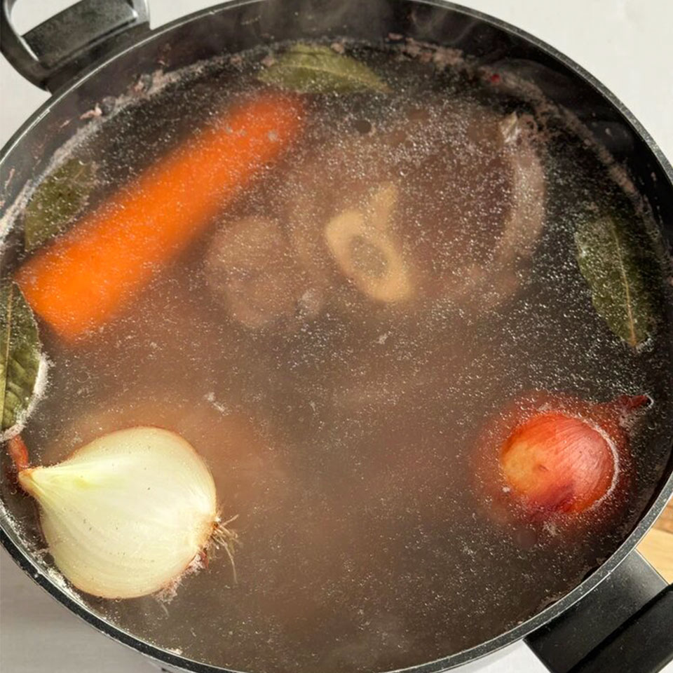 В кастрюлю с холодной водой поместите мясо, морковь, лук, лавровый лист и перец горошком и начните варить на среднем огне. Когда вода закипит, снимите пенку и томите бульон на слабом огне в течение 7 часов.
