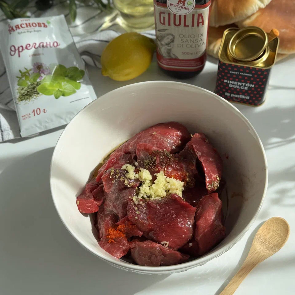 Добавьте к мясу паприку, орегано, соль, оливковое масло и пропущенный через пресс чеснок. Туда же выдавите сок лимона и перемешайте. Накройте мясо пищевой плёнкой и оставьте на 2–3 часа.