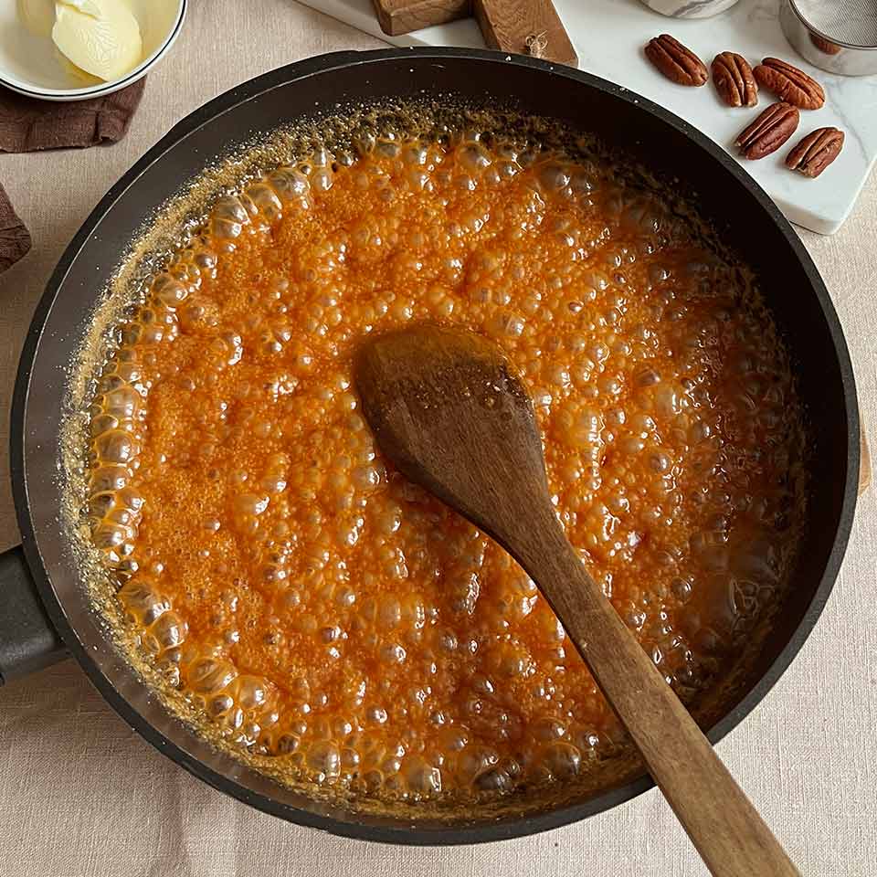 Снимите сковороду с огня, добавьте нарезанное кубиками сливочное масло. Хорошенько перемешайте. Масса начнёт пузыриться — это нормально. Подогрейте сливки, добавьте их в карамельную массу и перемешайте до однородности. Если карамель получилась слишком жидкой, снова отправьте её на огонь и помешивая, доведите до лёгкого загустения. Имейте в виду: карамель загустеет сильнее, когда остынет.