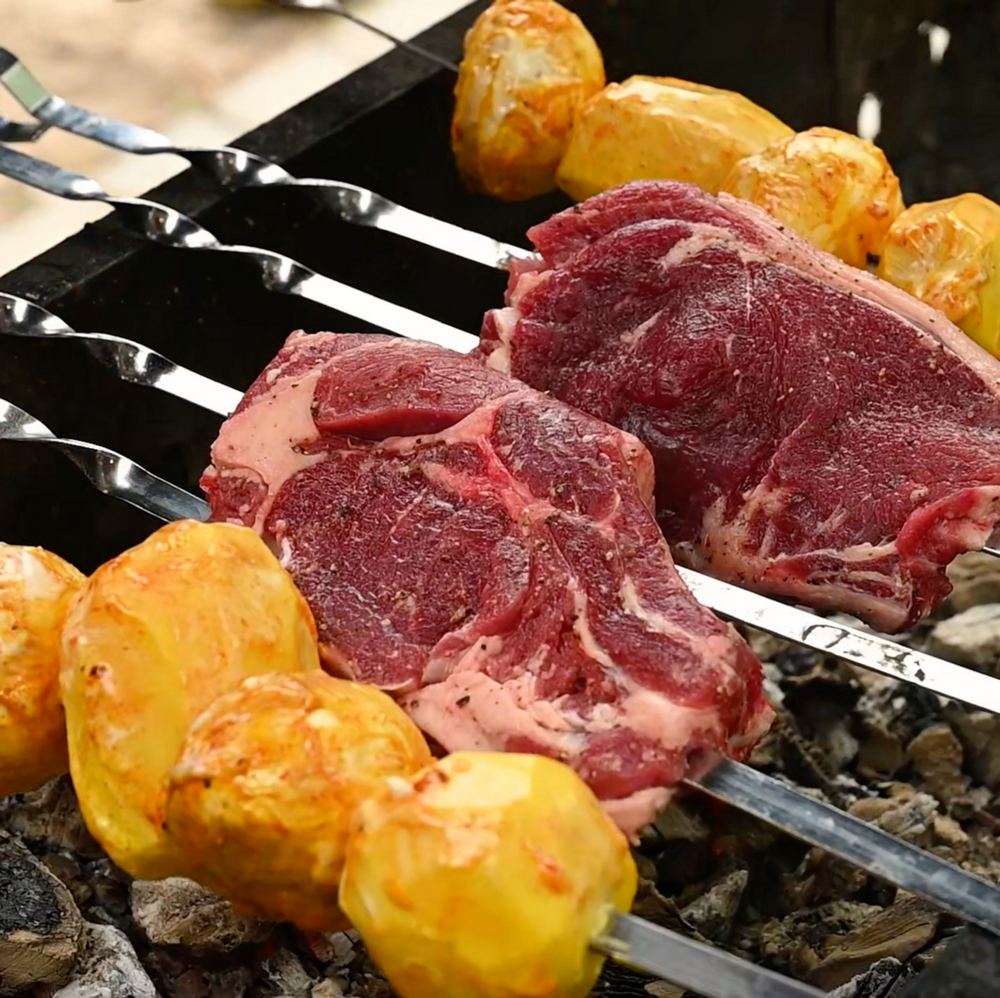 Стейки поперчите и посолите. Насадите мясо, картофель и шампиньоны на шампуры. Поджарьте на гриле стейки 20-25 минут, а картофель и шампиньоны — 30-35 минут