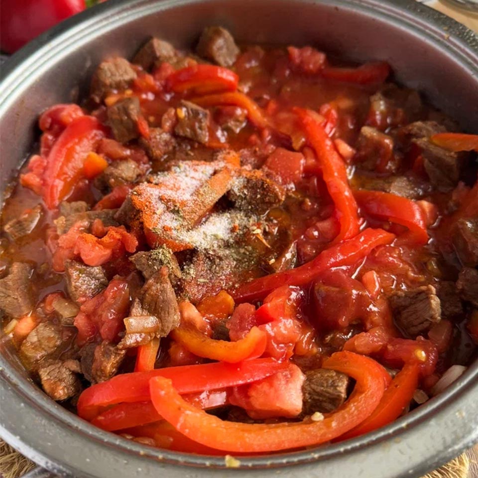 Добавьте к мясу овощи подготовленные овощи, а также томатную пасту, соль и специи. Накройте крышкой, снизьте огонь до среднего и тушите 10-15 минут.
